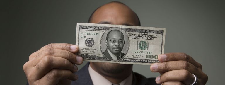 Man holding 100 dollar bill in front of face