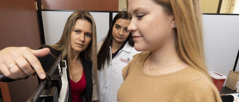 Associate professor Jamie Cooper shows graduate student Liana Rodrigues how to take height and weight of a subject for clinical health measures with undergraduate Allison Jones in Cooper’s clinical lab in Dawson Hall. (Photo by Andrew Davis Tucker/UGA)