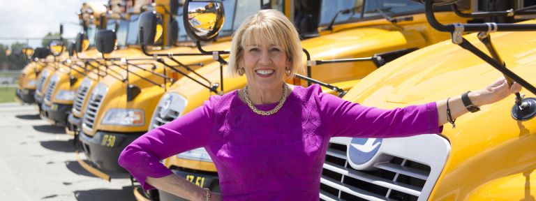 Woman in green dress in front of school buses